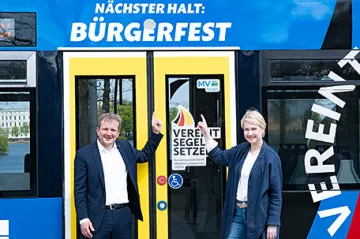 Schwerins IB Rico Badenschier und Bundesratspräsidentin Manuela Schwesig stehen vor den Türden der Straßenbahn und zeigen auf den Schriftzug Bürgerfest