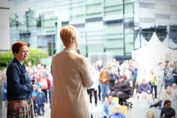 Manuela Schwesig steht mit dem Rücken zur Kamera auf einer Bühne und spricht zu Bürgerinnen und Bürgern.