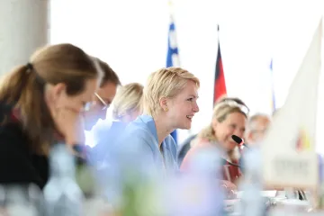 Manuela Schwesig spricht zu Menschen außerhalb des rechten Bildrandes. Sie ist umgeben von anderen Menschen, die in einem Tagungsraum an einer langen Tafel sitzen. 