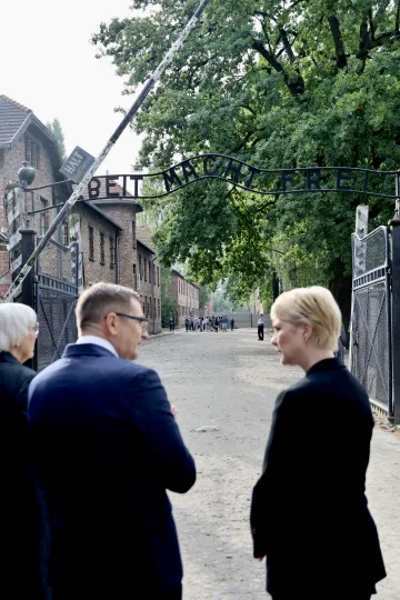 Manuela Schwesig in Begleitung eines Mannes auf der Eingangsstraße zu einem KZ. Darüber die Aufschrift „Arbeit macht frei". 