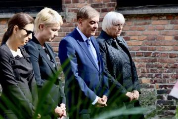 Manuela Schwesig steht mit drei anderen Personen auf einem Platz. Sie falten die Hände und senken den Blick.