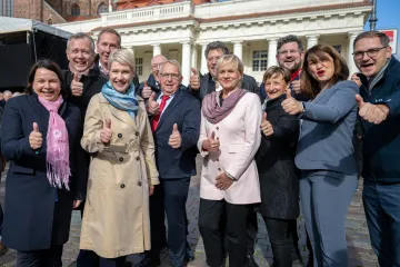 Das Bild zeigt eine Gruppe von Menschen, die alle gemeinsam fröhlich in die Kamera lächeln und den Daumen hochhalten. Im Zentrum der Gruppe steht Manuela Schwesig in einem beigen Mantel.